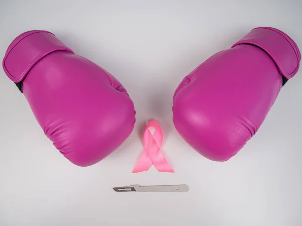 Pink boxing gloves, a surgical scalpel and a pink ribbon on a white background. The concept of fighting breast cancer