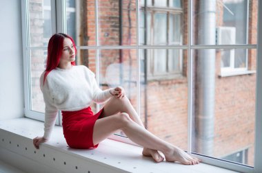 Cam kenarında oturan kızıl saçlı, beyaz bir kadın.