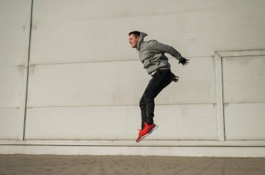 Kapüşonlu beyaz adam elleri dışarıda dizlerinin üzerinde yükseğe zıplıyor.