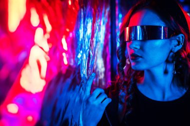 Beyaz tenli, güneş gözlüklü, neon ışıklı kadının folyo duvarına yakın plan portresi.