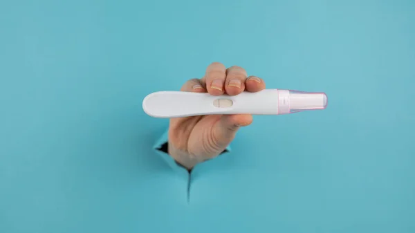 A hand with a negative pregnancy test sticking out of a hole in a blue cardboard background