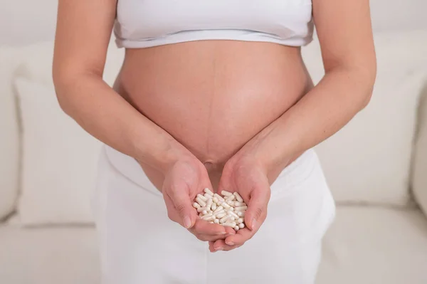A faceless pregnant woman is holding a handful of white pills