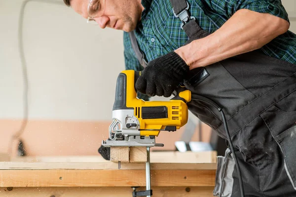 工房で電気ジグソーで木板を切る男 — ストック写真