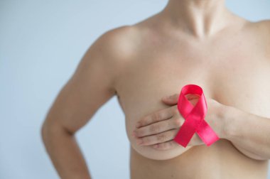 Beyaz bir arka planı olan beyaz bir kadın göğsünü kapatıyor. Pembe kurdele göğüs kanseriyle mücadeleyi sembolize ediyor.