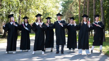 Group of graduates in robes dancing outdoors. Elderly student