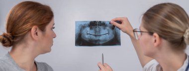 Resepsiyondaki bir kadın doktor ve bir hasta çene röntgenini tartışıyorlar.