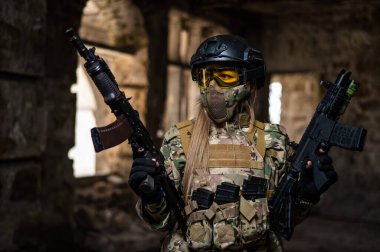 Askeri üniformalı bir kadın terk edilmiş bir binada silah tutuyor.