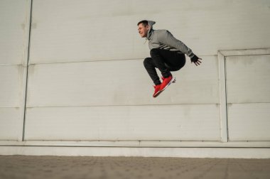 Kapüşonlu beyaz adam elleri dışarıda dizlerinin üzerinde yükseğe zıplıyor.