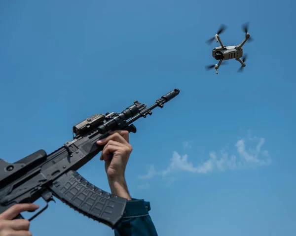 A man aims to shoot a rifle at a flying drone against a blue sky