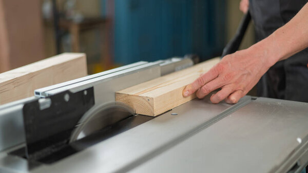 Close-up of a man cutting a wooden board on a circular machine