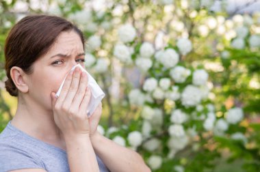 Çiçek açan bir bahçede orta yaşlı bir kadın burnunu siliyor.
