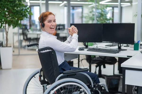 Caucasian woman with headset in a wheelchair. Happy female call center worker in the office