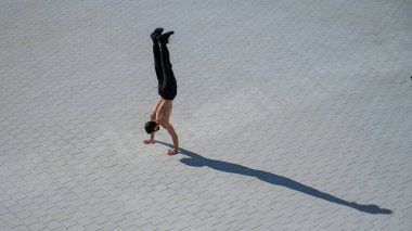 Tişörtsüz bir adam dışarıda elini kolunu sallayarak yürüyor. Yukarıdan görüntüle