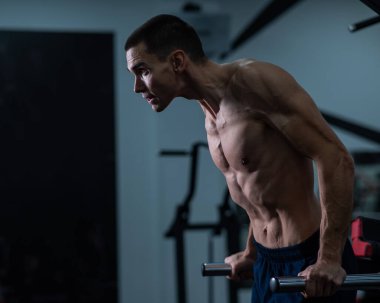 Shirtless man doing triceps dips from parallel bars in gym