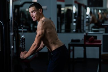 Shirtless man doing triceps pulldown at the gym