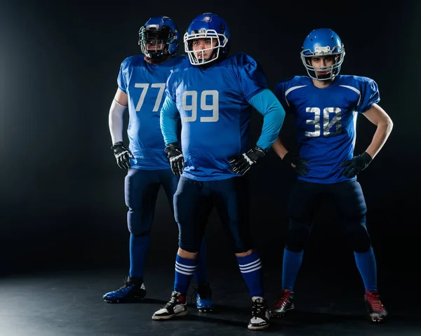 Portrait of three men in blue uniforms for American football on a black background