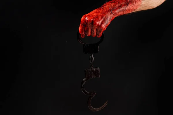 Faceless man holding handcuffs black background. Hands are stained with blood
