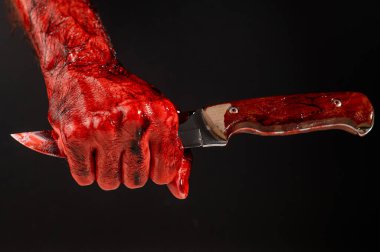 Eli kanlı bir adam siyah bir arka planda bıçağın ucunu tutuyor.