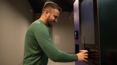 Kafkasyalı bir adam otomattan kendine kahve dolduruyor.