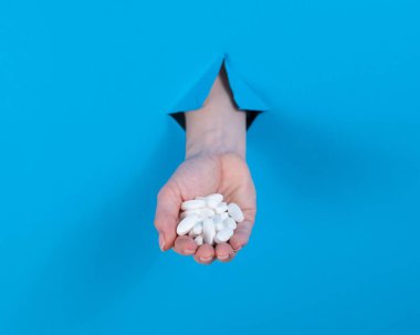 Bir kadın bir avuç dolusu hap tutuyor. Bir kadın elleri karton mavi bir arka planda bir delikten sarkıyor.