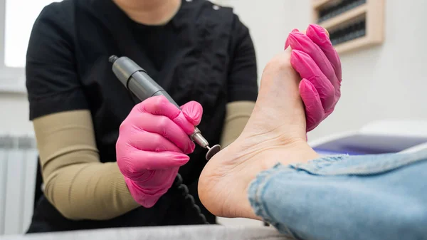 A pedicurist treats the heels of a client using a machine with an abrasive disc in a beauty salon