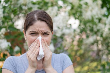 Beyaz kadın alerji hastası ve parkta yürürken burnunu peçeteye sümkürmüş.