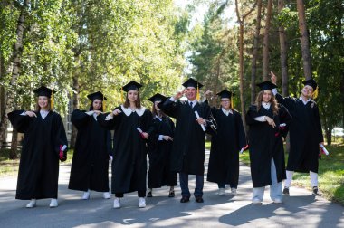Group of graduates in robes dancing outdoors. Elderly student