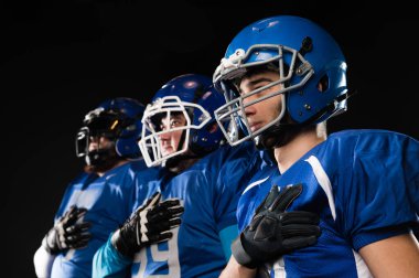 Portrait of three men in blue uniforms for American football with a hand on his chest on a black background