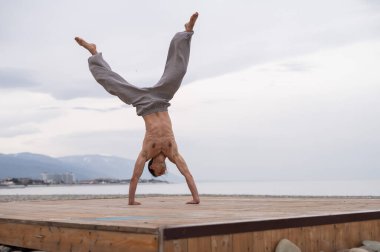 Üstsüz beyaz adam sahilde akrobatik tekerlek yapıyor.