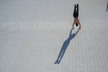 Tişörtsüz bir adam dışarıda elini kolunu sallayarak yürüyor. Yukarıdan görüntüle