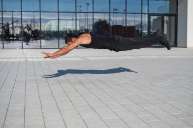 Siyah spor kıyafetli bir adam dışarıda şınav çekerken zıplıyor.