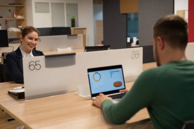 Kızıl saçlı beyaz kadın ve sakallı adam açık uzay ofisinde çalışıyor.