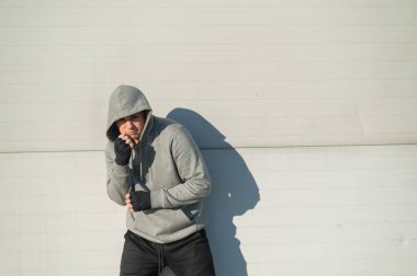 Kapüşonlu bir adam gri bir duvara karşı boks antrenmanı yapıyor.