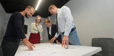 Four business people review and discuss blueprints. Designers engineers at a meeting