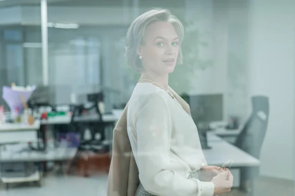 stock image Portrait of a beautiful gray-haired caucasian woman in the office standing behind a glass wall