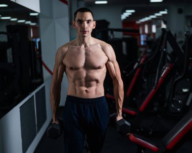 Shirtless man doing bicep exercises with dumbbells in the gym