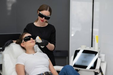 Gözlüklü bir kanepede bir kadın fotorojenizasyon ameliyatı oluyor. Donanım kozmetolojisi