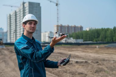 Kasklı ve tulumlu bir adam inşaat alanındaki bir dronu kontrol ediyor. İnşaatçı teknik bir hata yapıyor.