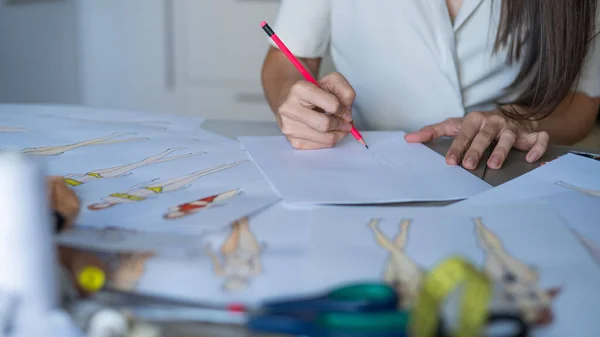 stock image Faceless woman draws sketches of swimwear with a pencil. Close-up of the hands of a fashion designer