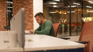 Modern çalışma alanında dizüstü bilgisayarda çalışan beyaz sakallı bir adam.