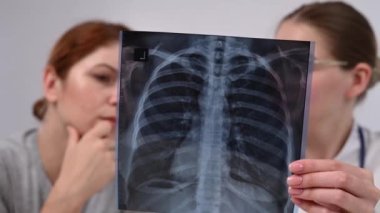 Doktor beyaz bir kadına danışıyor ve akciğerlerin röntgenleri hakkında yorum yapıyor.