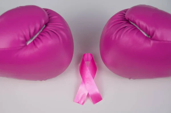 Pink boxing gloves and pink ribbon on a white background. The concept of the fight against breast cancer