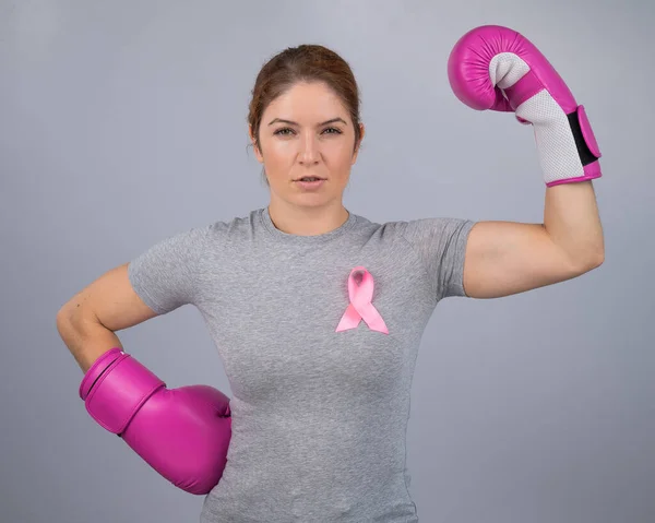 A woman with a pink ribbon on her chest in pink boxing gloves on a gray background. Victory over breast cancer