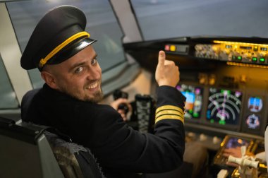 Uçuş simülatörü kullanırken gülümseyen beyaz sakallı bir adam. Pilot kokpitte baş parmak gösteriyor.