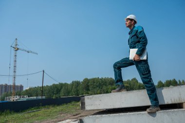 İnşaat alanında elinde dizüstü bilgisayar tutan beyaz erkek müteahhit.