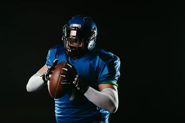 An Asian man with a red beard in a blue American football uniform throws a ball against a black background