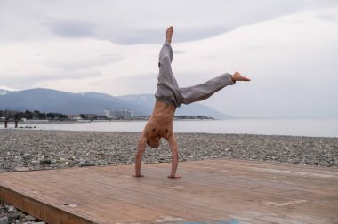 Üstsüz beyaz adam sahilde akrobatik tekerlek yapıyor.