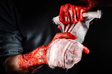 Kanla kaplı bir adam ellerini bandajlıyor.
