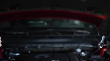 Kadın elinin baş parmağı yukarıda, tamircinin eli de aletle. Eldivenlerdeki otomotiv ustası işi bitirdikten sonra olumlu bir hareket gösteriyor.