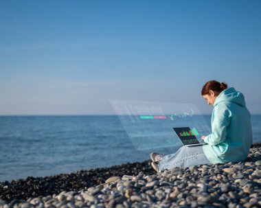 Beyaz kadın deniz kıyısında oturuyor ve dizüstü bilgisayarla çalışıyor. Yüksek çözünürlük menüsü. Borsa tabloları. Komisyon terminali